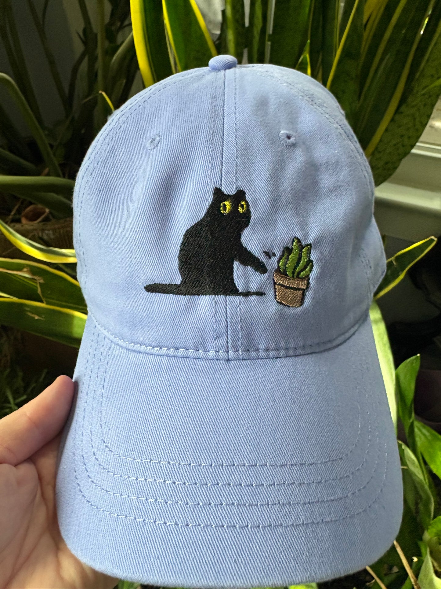 Cat knocking over plant embroidered on light purple cotton dad hat