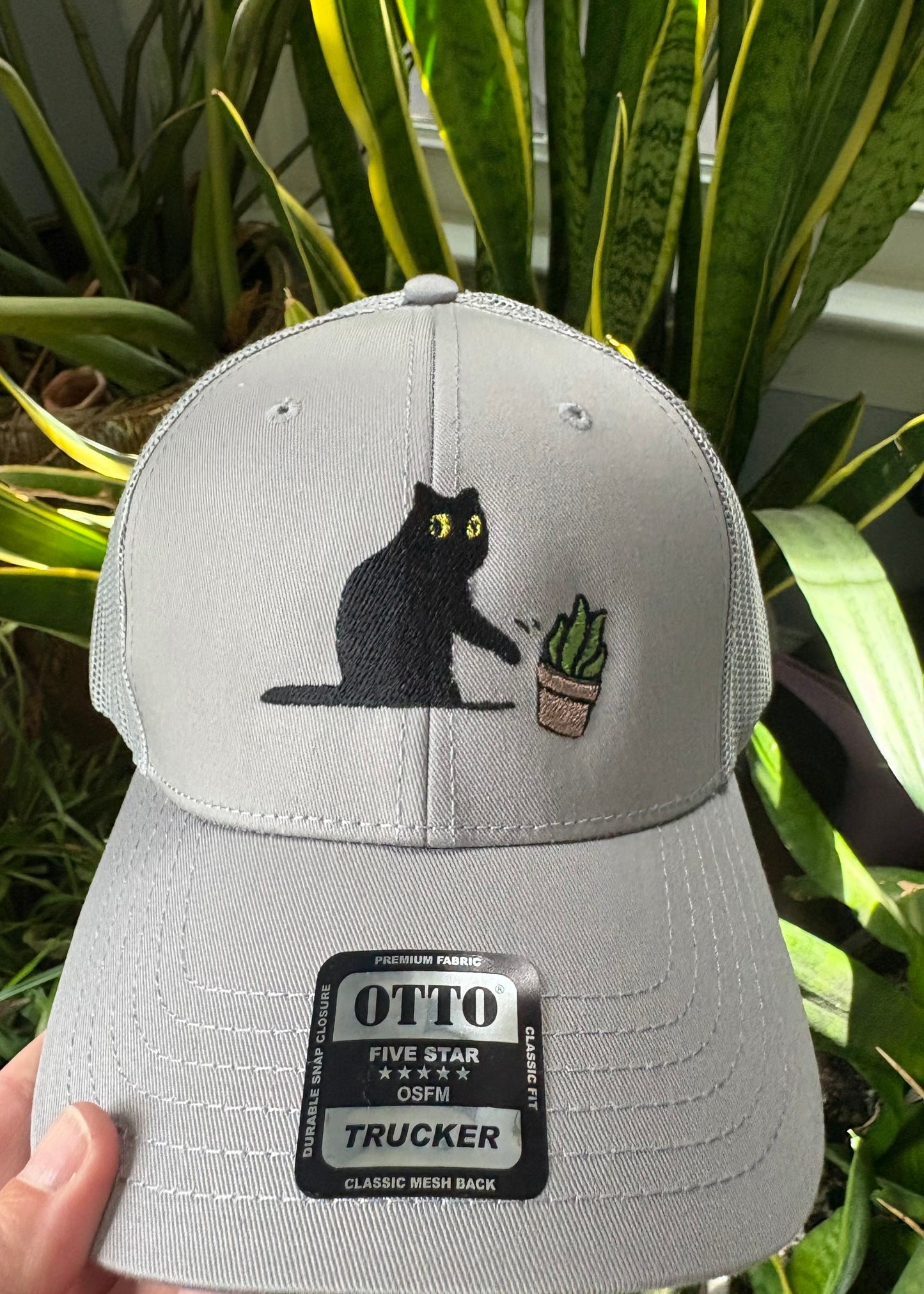 Cat knocking over plant embroidered on light grey Otto trucker hat