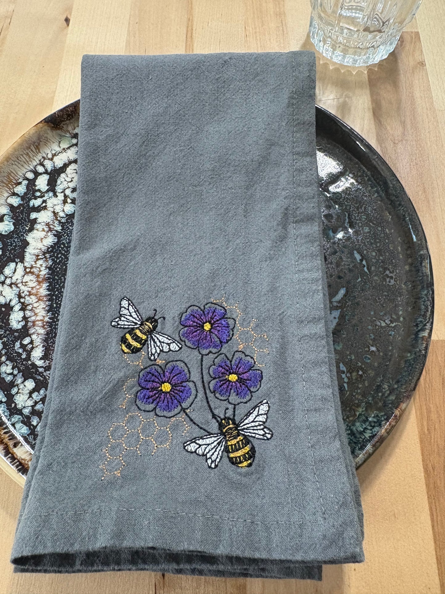 Gray napkin with embroidered bees and violets on a wooden surface