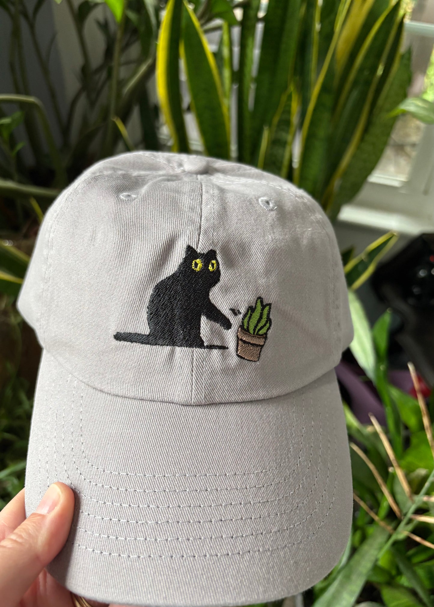 Cat knocking over plant embroidered on light grey dad hat