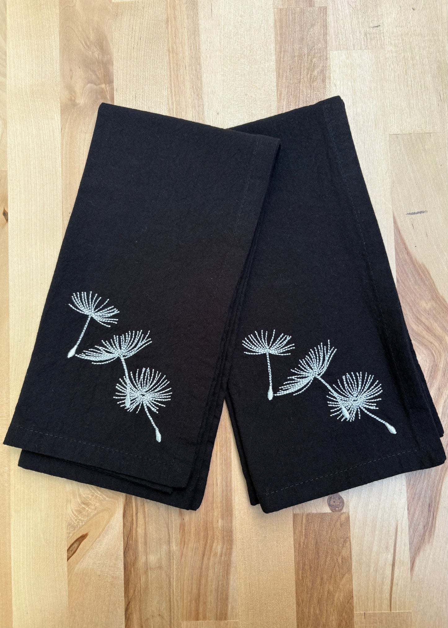Add a touch of whimsy to your table with these black dinner napkins adorned with delicate silver dandelion puffs. Their dark color cleverly hides stains, keeping your setting looking sharp through every course. Machine washable for easy care, these napkins blend elegance with practicality, making every meal feel a little more magical.