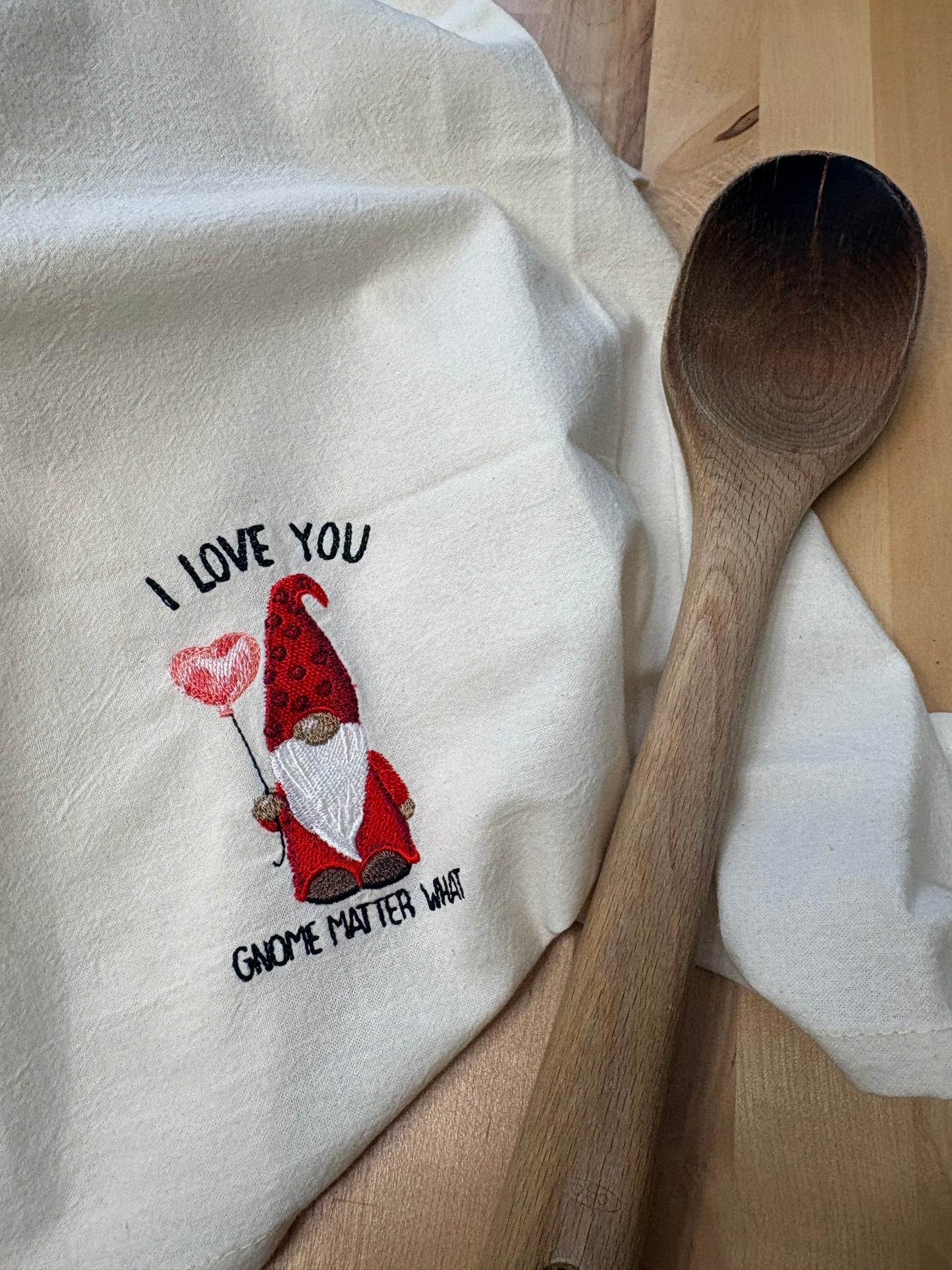 White towel with embroidered gnomes and text, wooden spoon on top