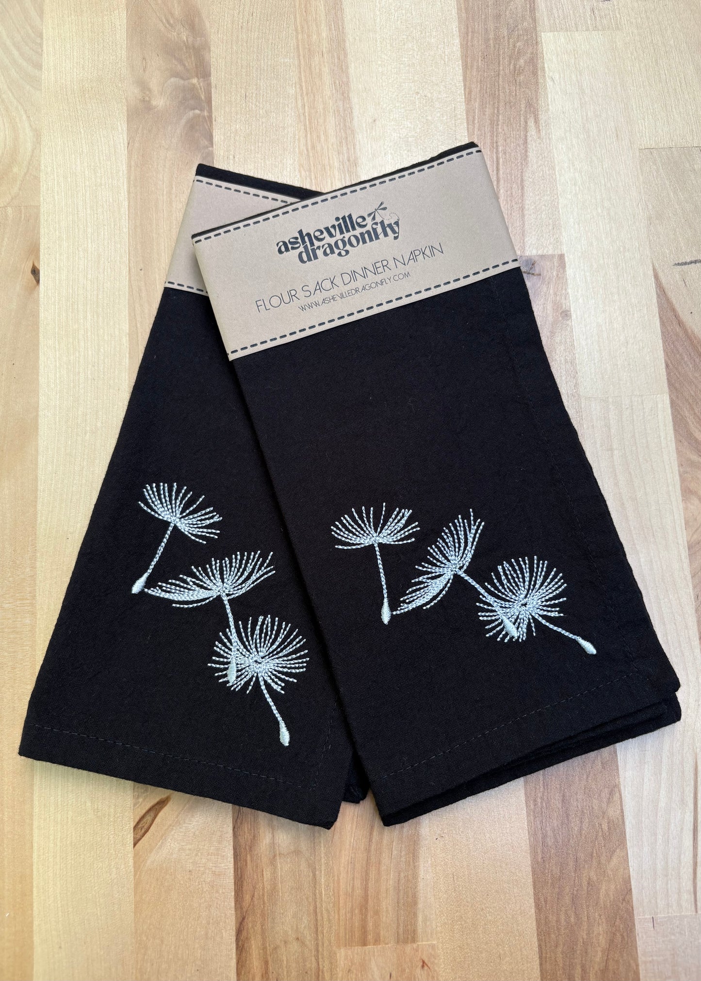 Add a touch of whimsy to your table with these black dinner napkins adorned with delicate silver dandelion puffs. Their dark color cleverly hides stains, keeping your setting looking sharp through every course. Machine washable for easy care, these napkins blend elegance with practicality, making every meal feel a little more magical.