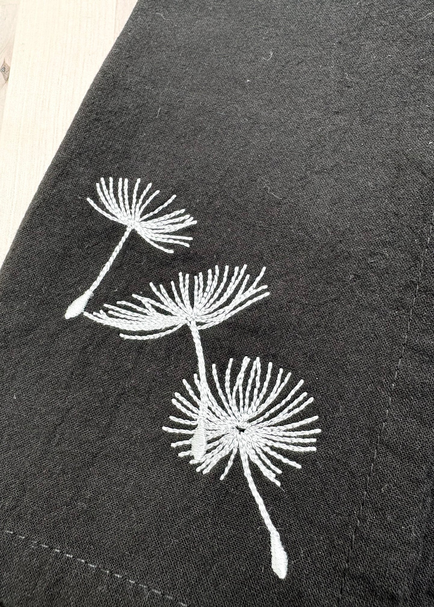 Add a touch of whimsy to your table with these black dinner napkins adorned with delicate silver dandelion puffs. Their dark color cleverly hides stains, keeping your setting looking sharp through every course. Machine washable for easy care, these napkins blend elegance with practicality, making every meal feel a little more magical.