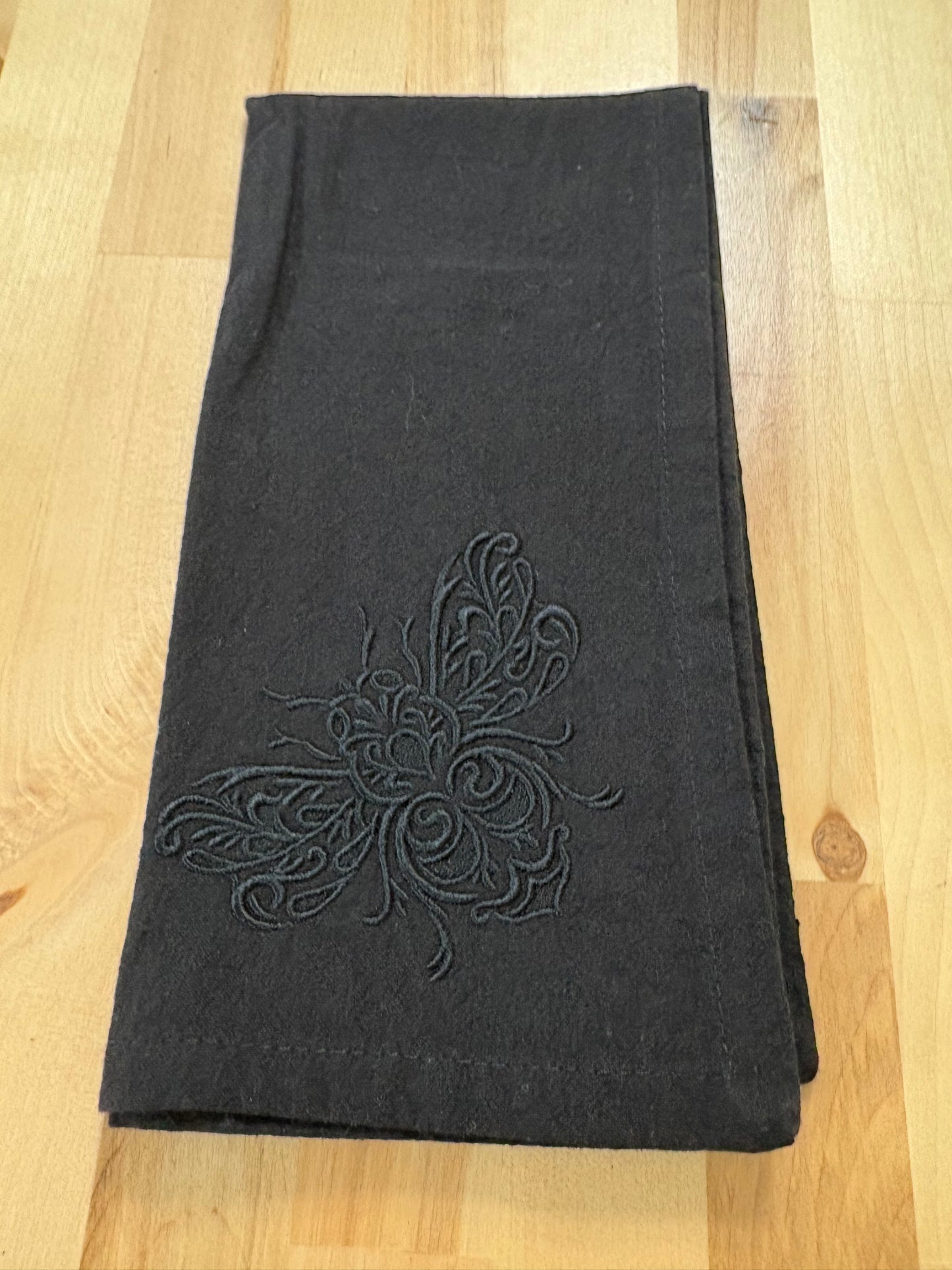 Delicate bee embroidered on black napkin with black thread