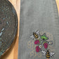 Gray towel with embroidered bees and raspberries on a wooden surface