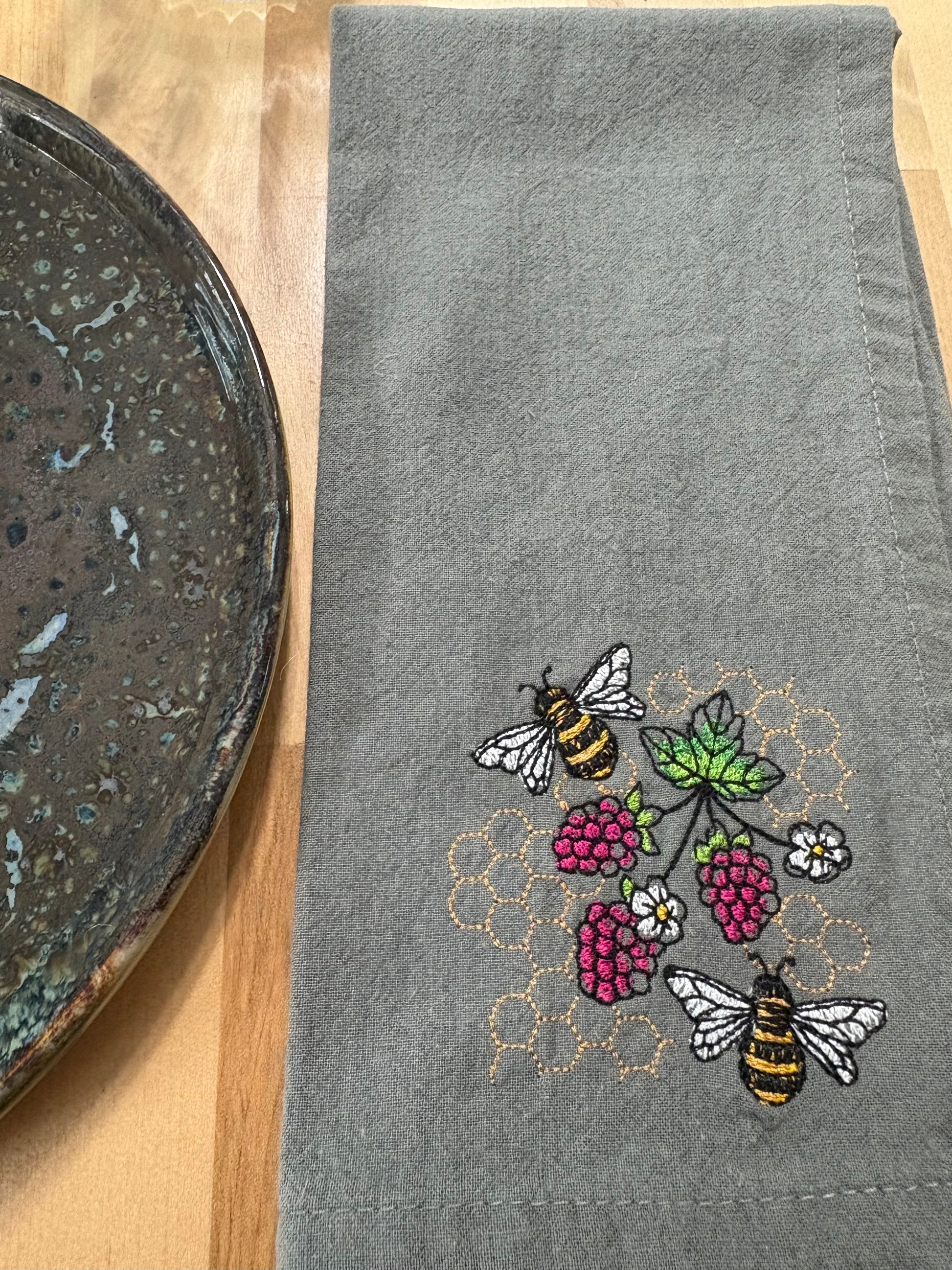Gray towel with embroidered bees and raspberries on a wooden surface