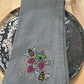 Gray embroidered napkin with bee and raspberry design on a wooden surface
