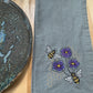 Embroidered gray towel with bees and violets on a wooden surface
