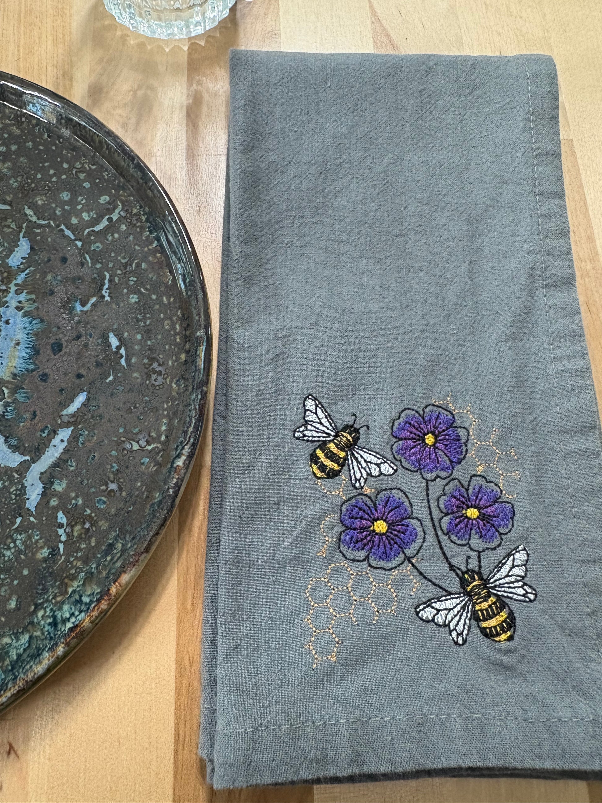 Embroidered gray towel with bees and violets on a wooden surface