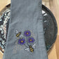 Gray napkin with embroidered bees and violets on a wooden surface