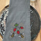 Gray embroidered napkin with bees and strawberries on a wooden surface