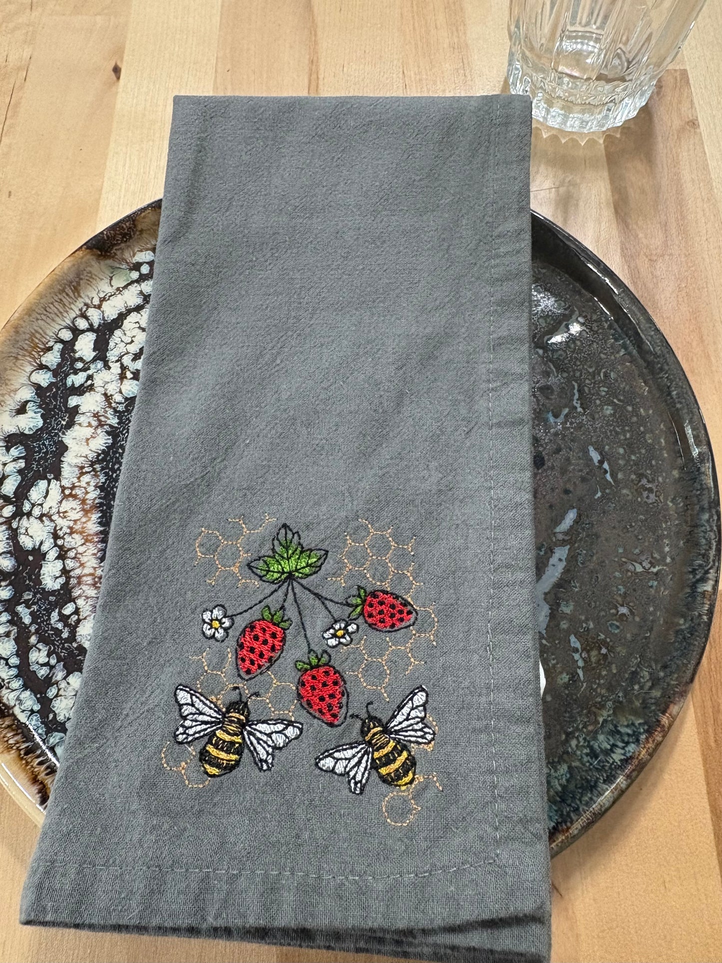 Gray embroidered napkin with bees and strawberries on a wooden surface