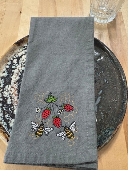 Gray embroidered napkin with bees and strawberries on a wooden surface