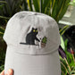 Cat knocking over plant embroidered on light grey dad hat