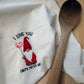 White towel with embroidered gnomes and text, wooden spoon on top
