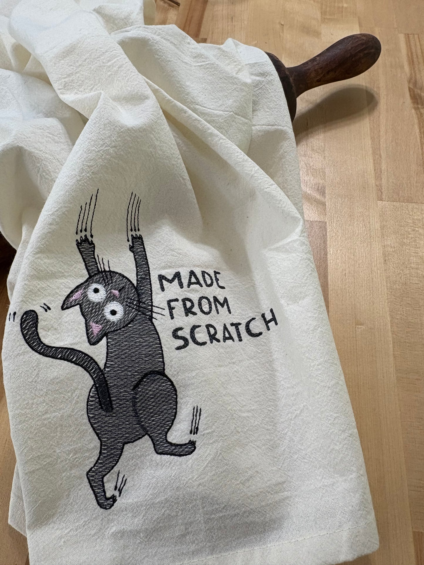 White towel with a black cat illustration and text 'Made from Scratch' on a wooden surface.