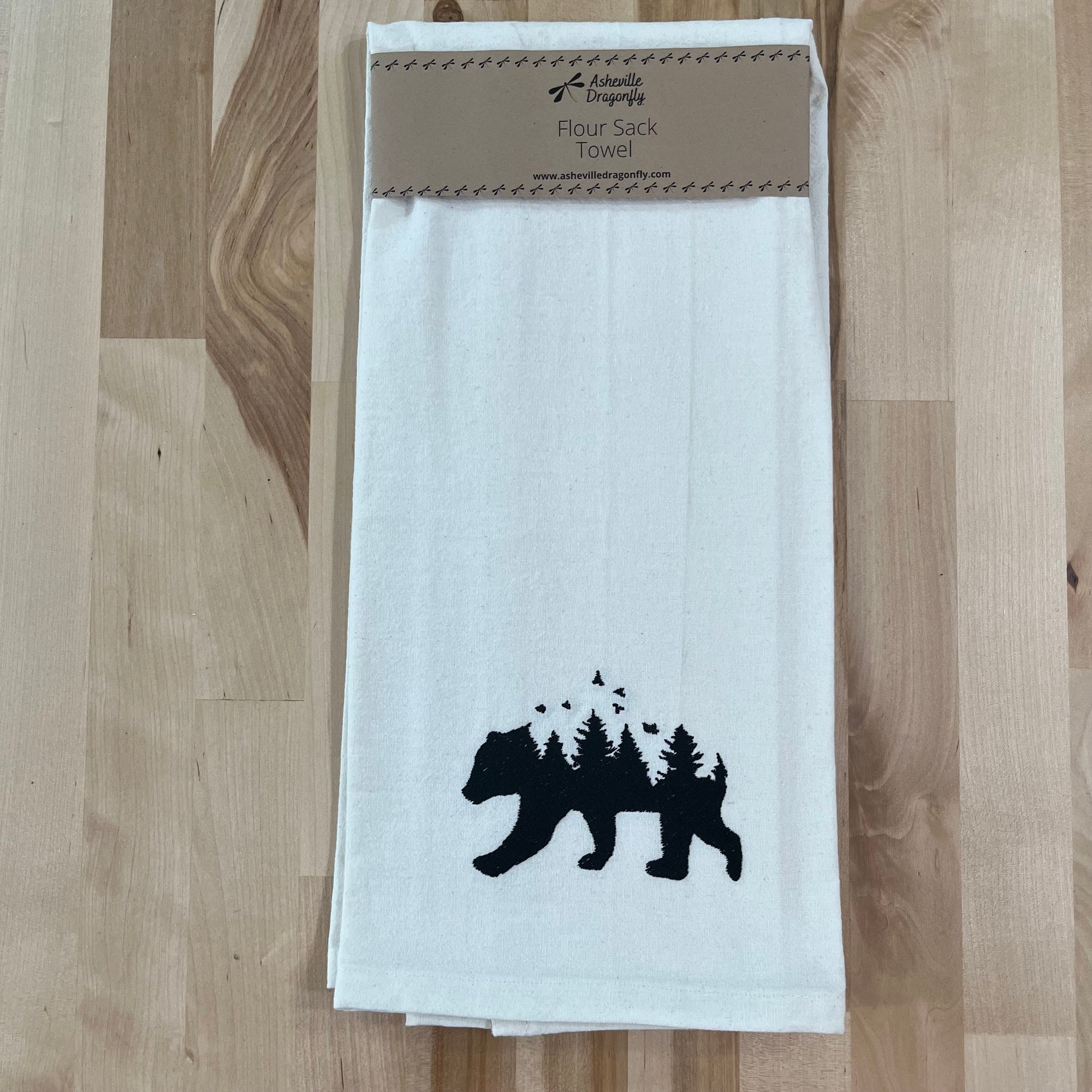 A white kitchen towel with black embroidery of a bear and trees on the lower part.