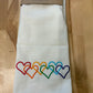 Folded white towel with rainbow-colored heart designs on a wooden surface