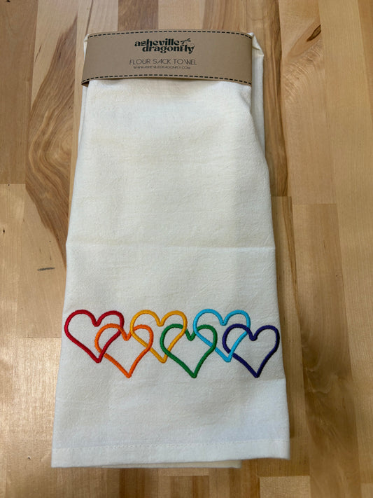 Folded white towel with rainbow-colored heart designs on a wooden surface