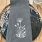 White dandelion embroidered on grey napkin