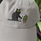 Cat knocking over plant embroidered on light grey dad hat